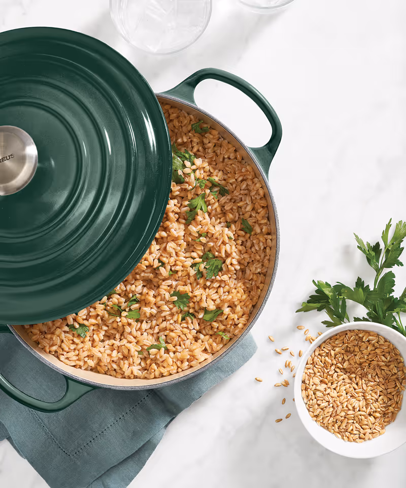 An overhead angle of a green Le Creuset Dutch oven full of cooked farro and a bowl of uncooked farro off to the side.