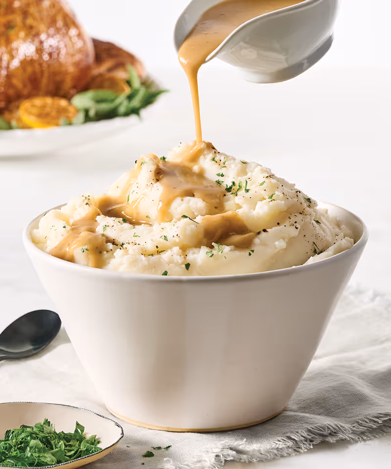 A bowl of mashed potatoes with gravy being poured on top.