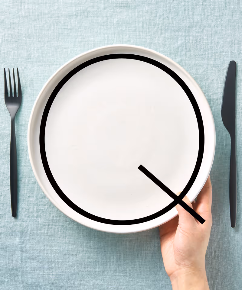 A hand setting a white plate on a surface between a fork and knife.