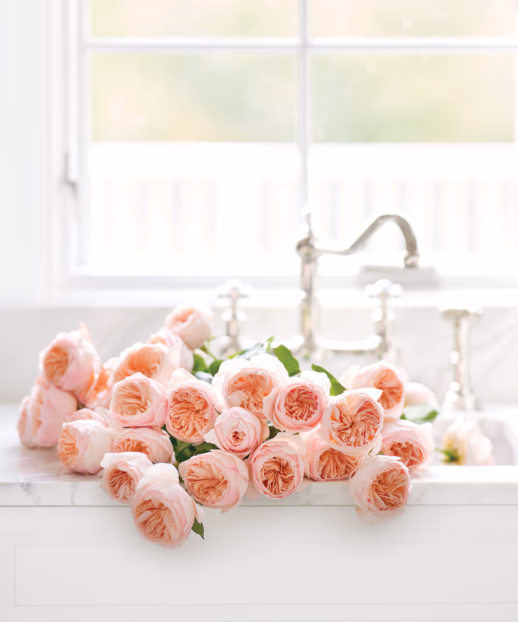 A white kitchen sink filled with pink blooming flowers.