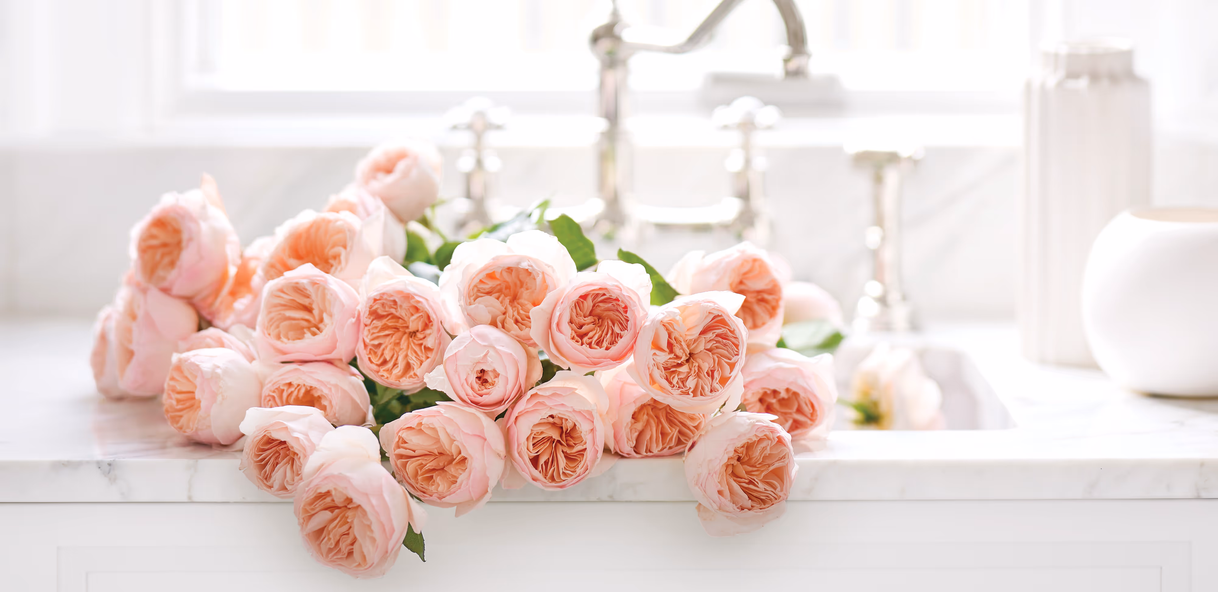 A white kitchen sink filled with pink blooming flowers.