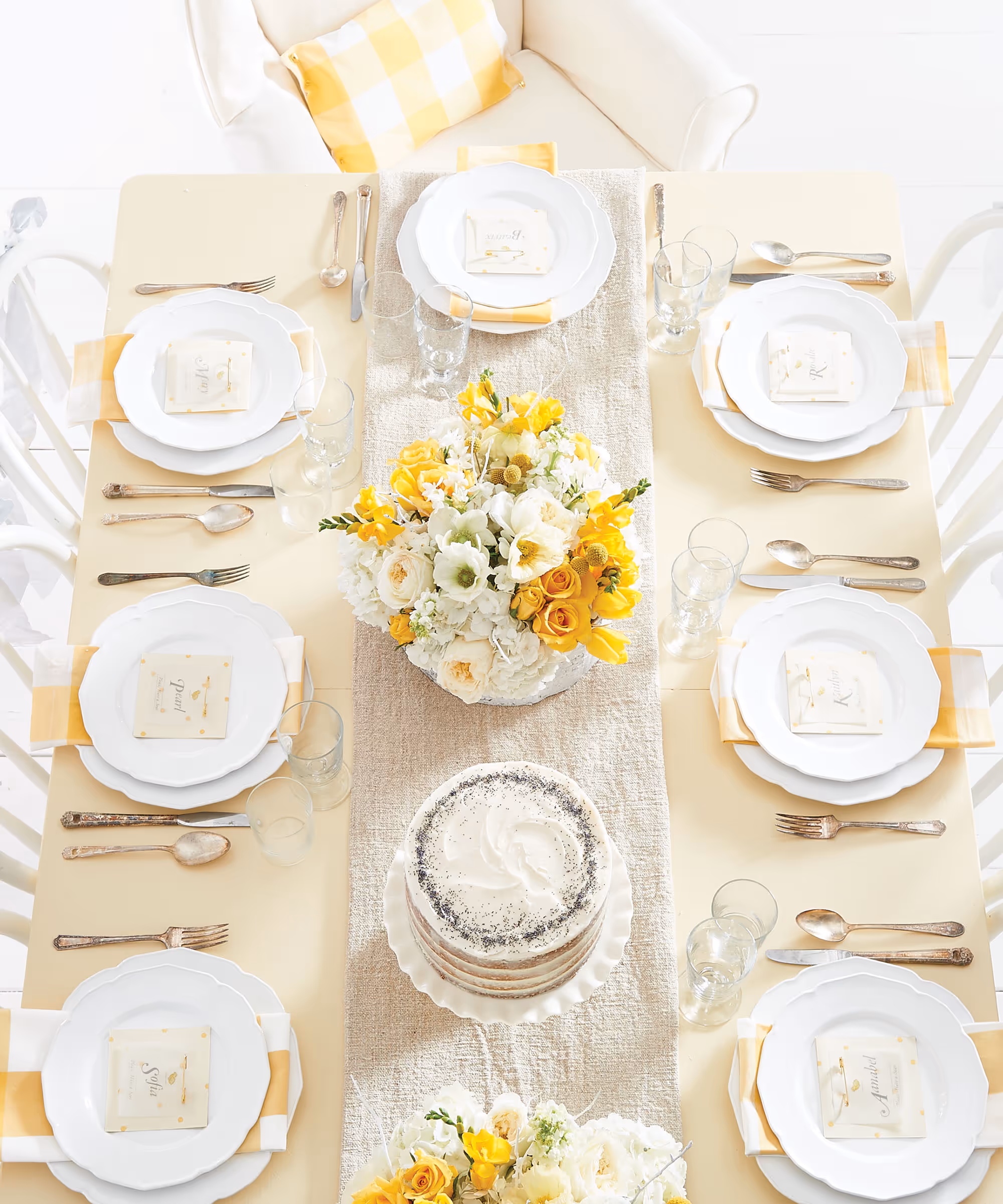 An overhead angle of a dining table dressed up with place settings, dinnerware sets, and yellow and white flower bouquets.