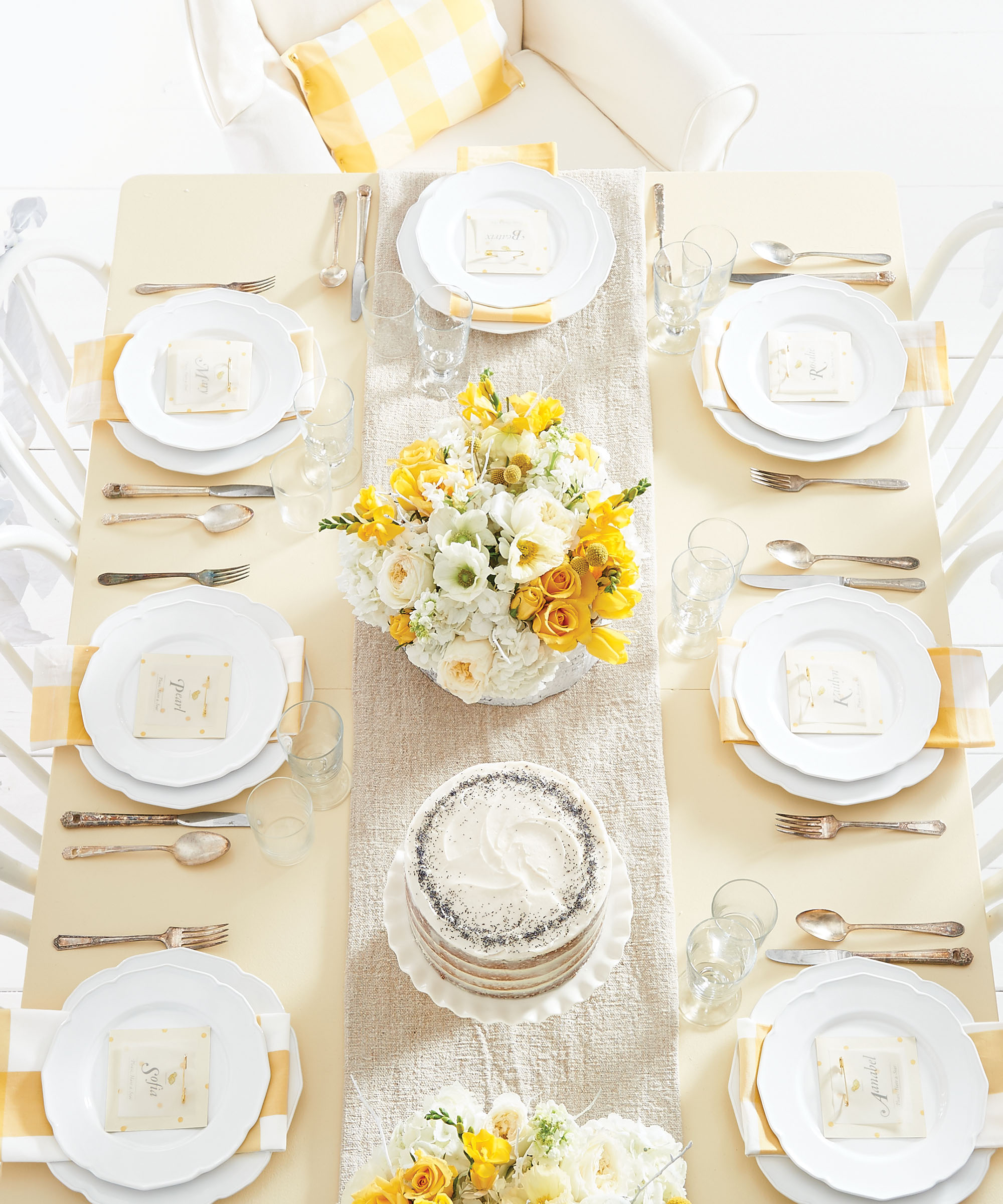 An overhead angle of a dining table dressed up with place settings, dinnerware sets, and yellow and white flower bouquets.