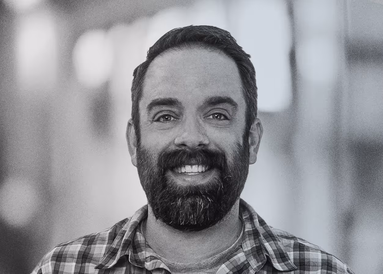Black and white portrait of a man with glasses and a beard, smiling at the camera.