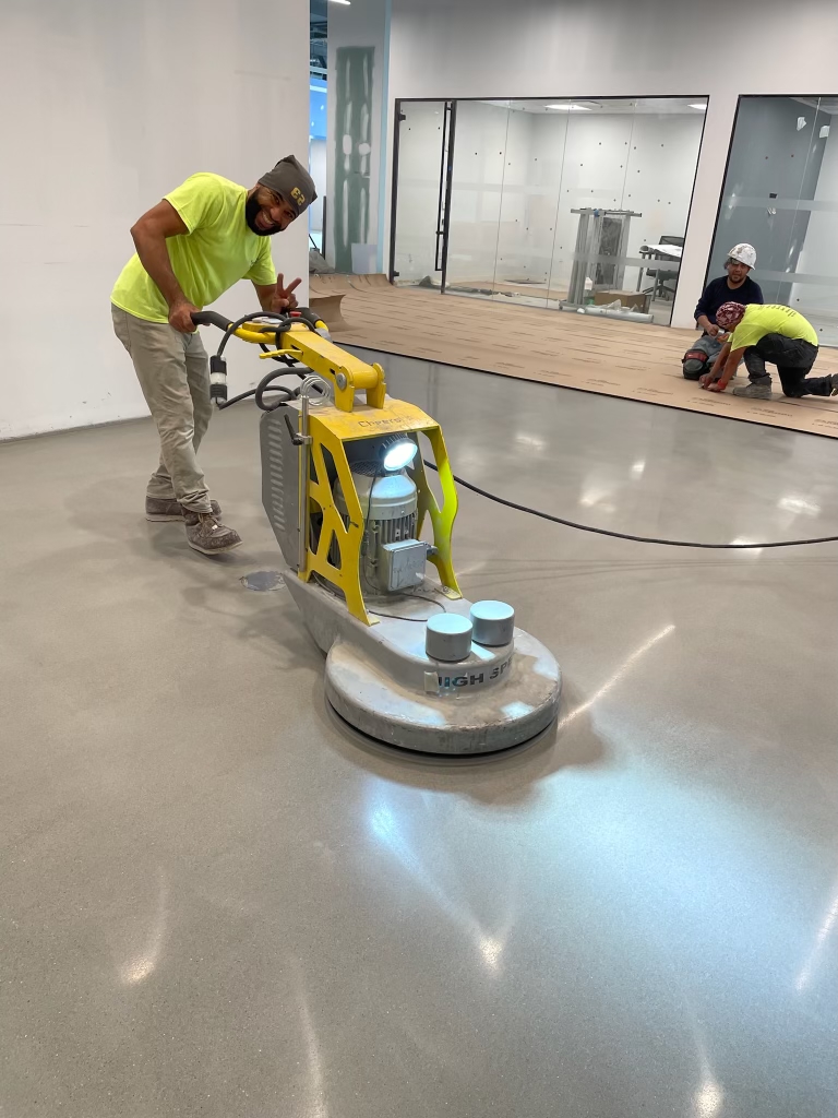 Man smiling at camera holding up peace sign while grinding concrete floor. 