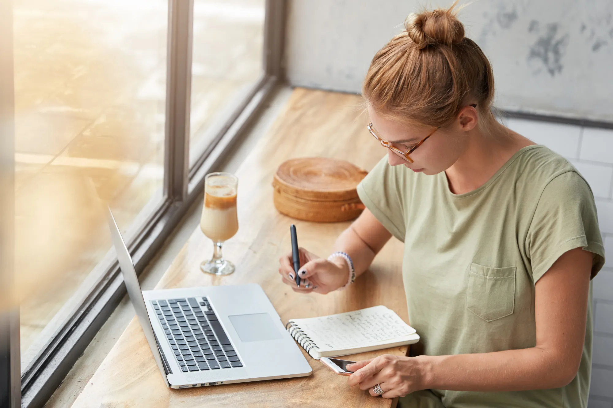 Une personne qui rédige sur son ordinateur portable et prend des notes à la main sur un carnet