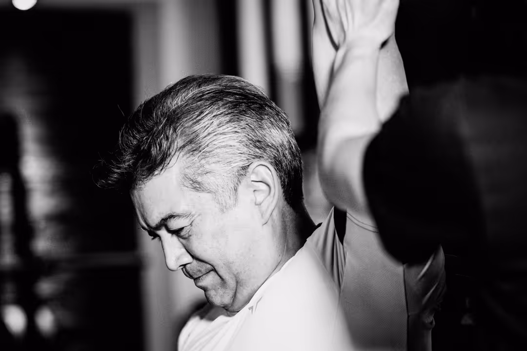 Profile of a middle-aged man with gray hair raising his arms, captured in black and white.