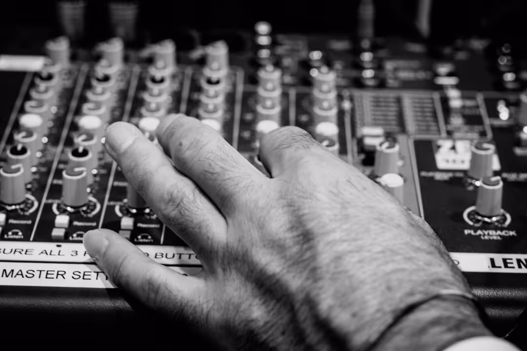Close-up of a hand adjusting knobs on a sound mixing console in black and white.