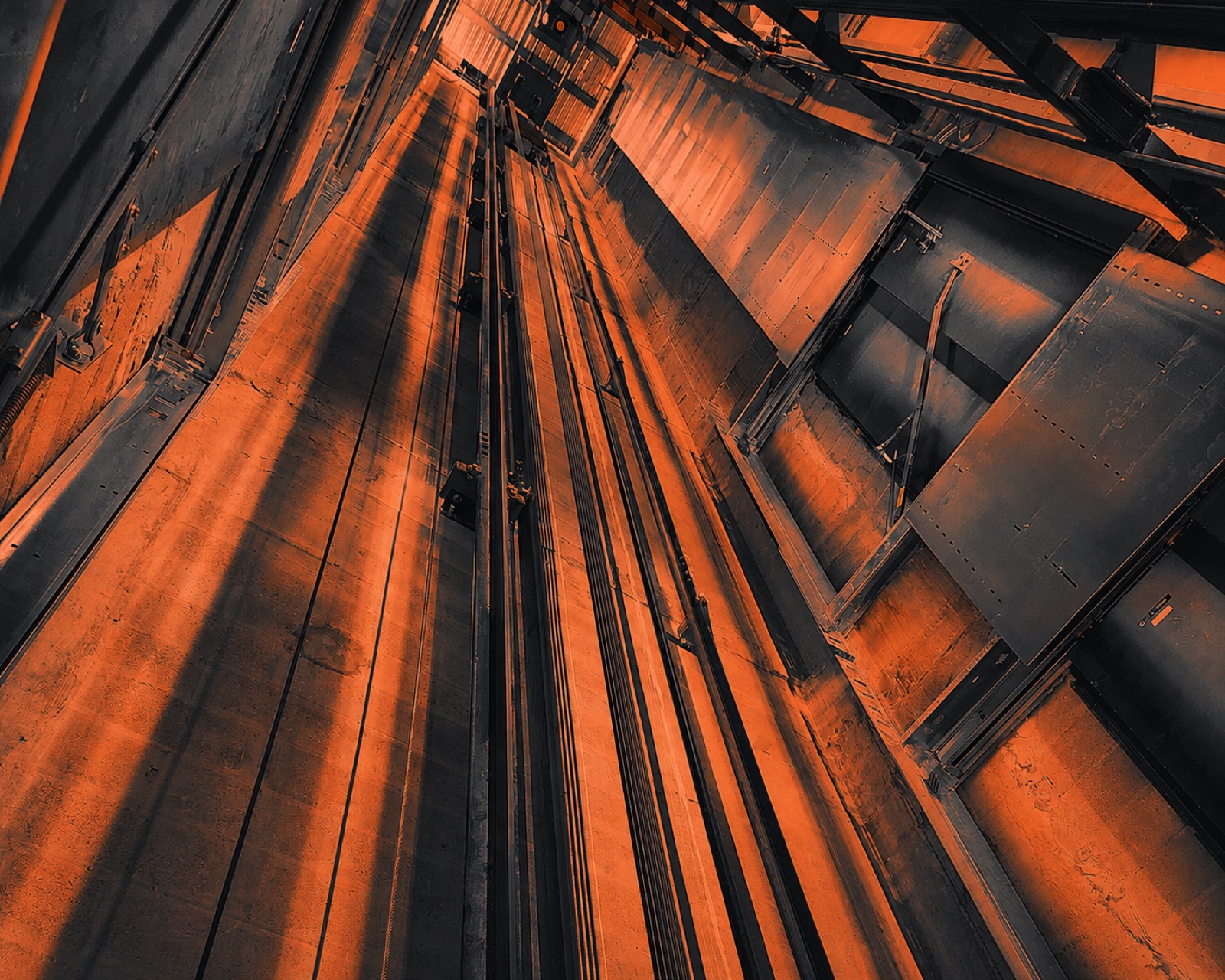 Upward view inside an elevator hoistway showing guide rails and structural steel lit in warm tones before an equipment removal
