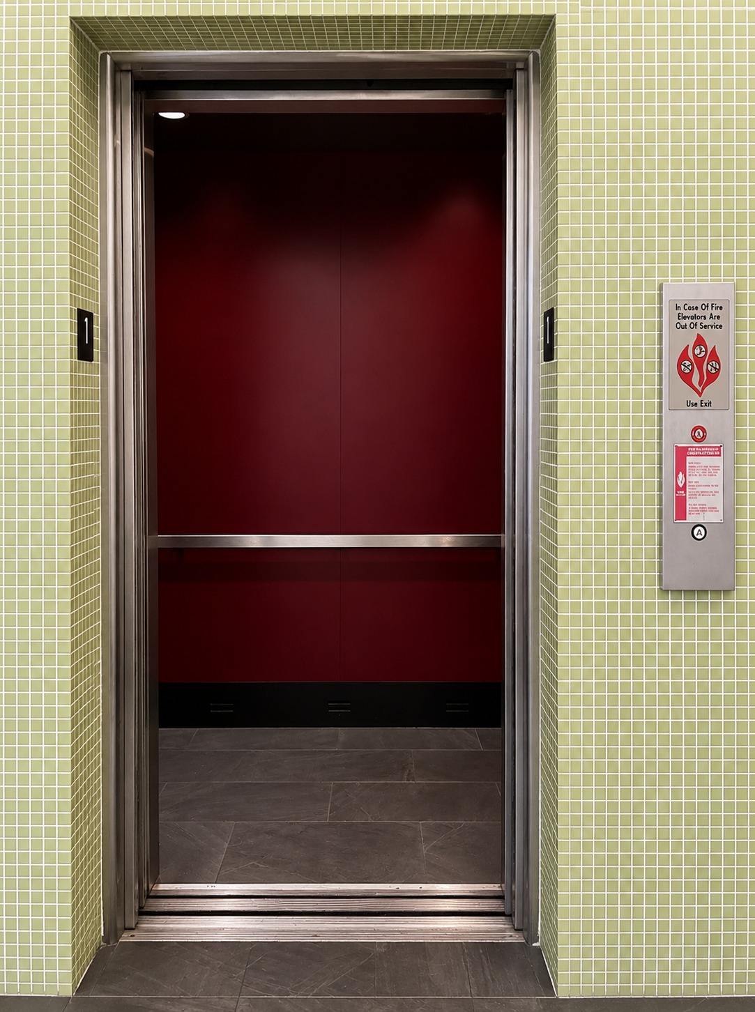 Elevator entrance with green mosaic tile surround and red cab interior at a Coconut Grove commercial building