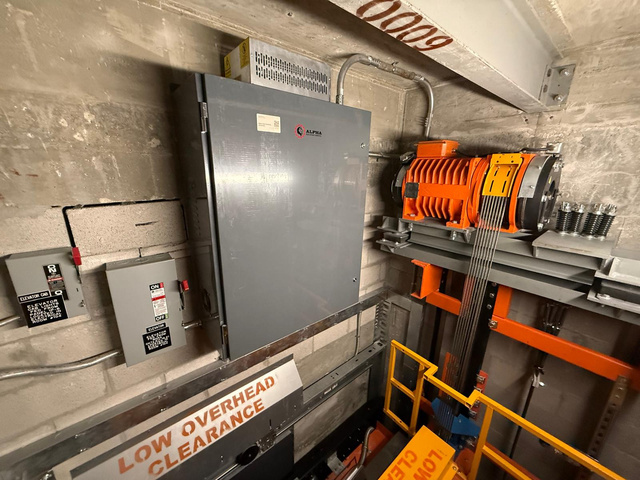 New Alpha elevator control cabinet and orange MRL traction machine in the machine room at Mater East Academy