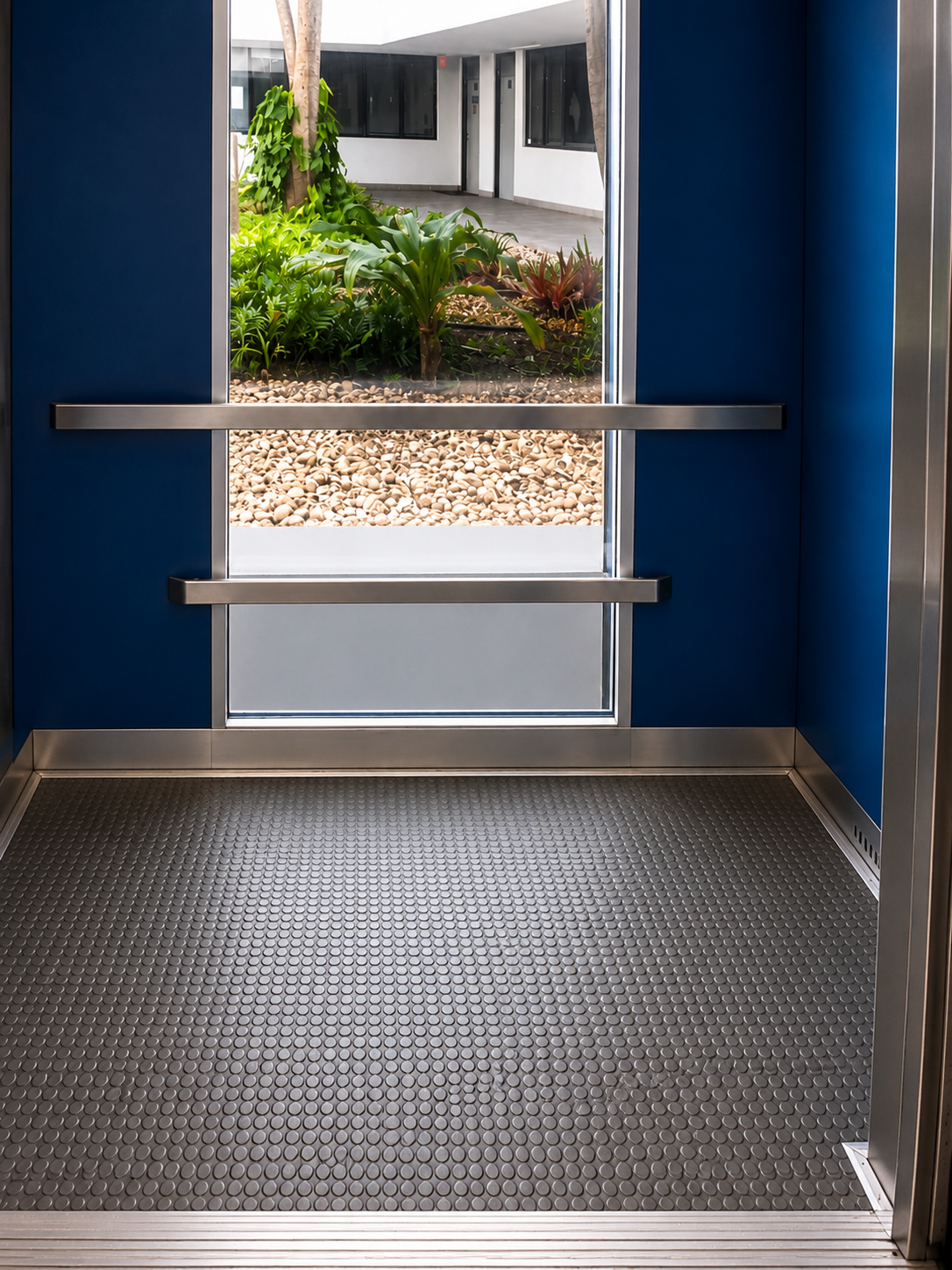 Panoramic glass elevator cab with deep blue walls and stainless handrails overlooking a landscaped courtyard at Flagler Wood in Miami