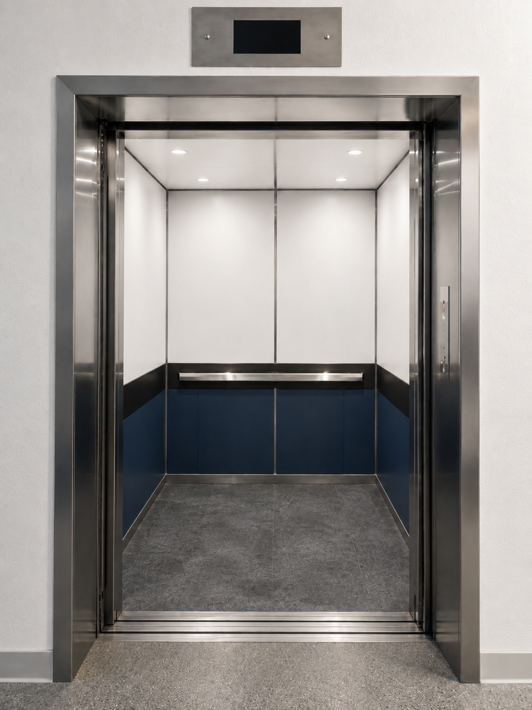 New elevator cab with white upper panels, navy blue lower panels, stainless handrail and stone tile floor at Cristo Rey Miami
