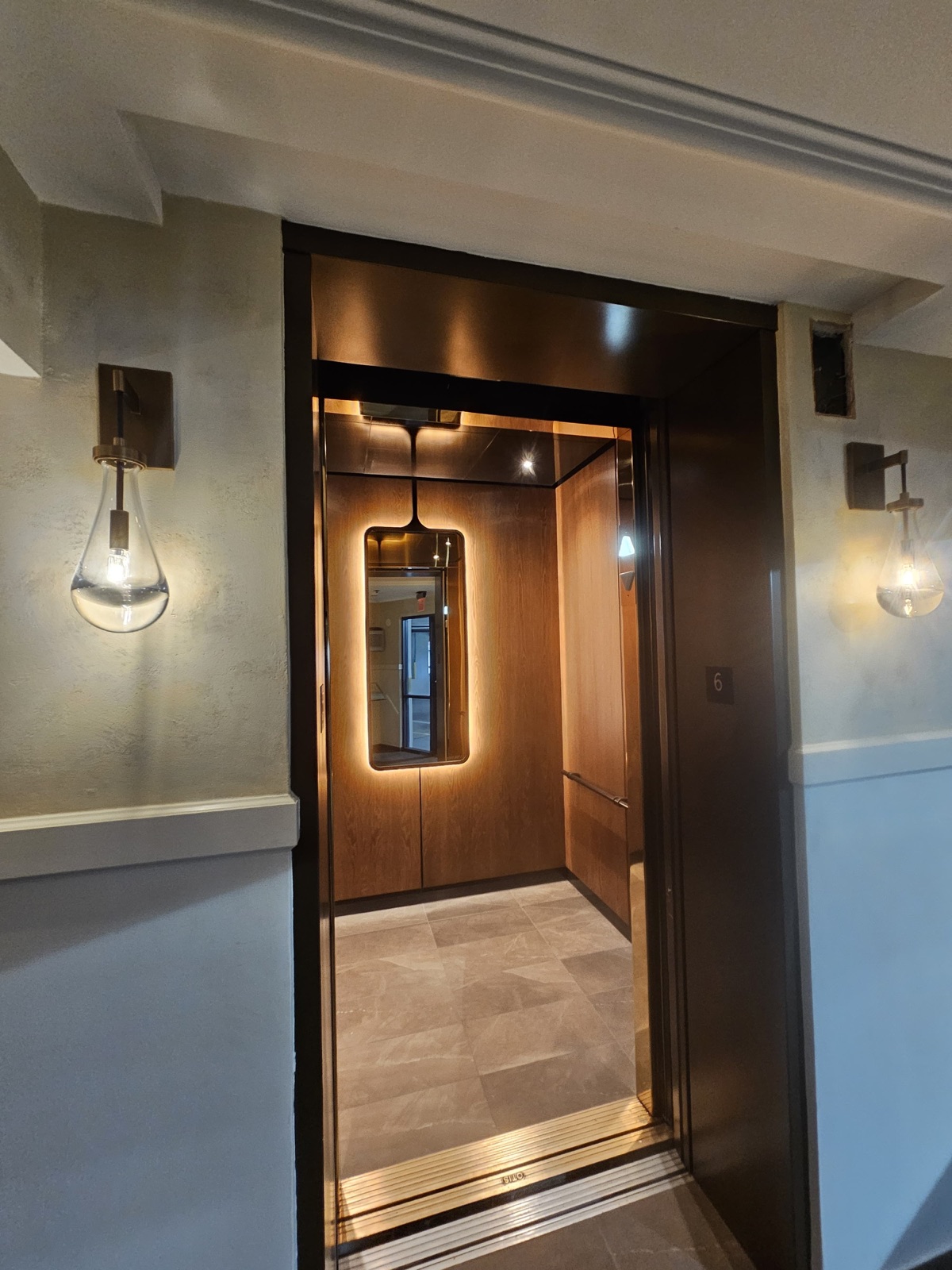 Modernized elevator cab with wood paneling, a backlit mirror and bronze finishes at 121 Alhambra