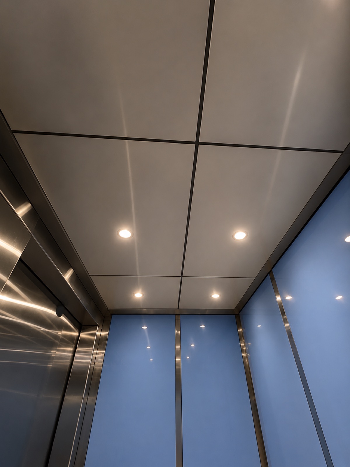 Elevator cab ceiling with recessed lighting and blue glass wall panels at Prestige District in North Miami