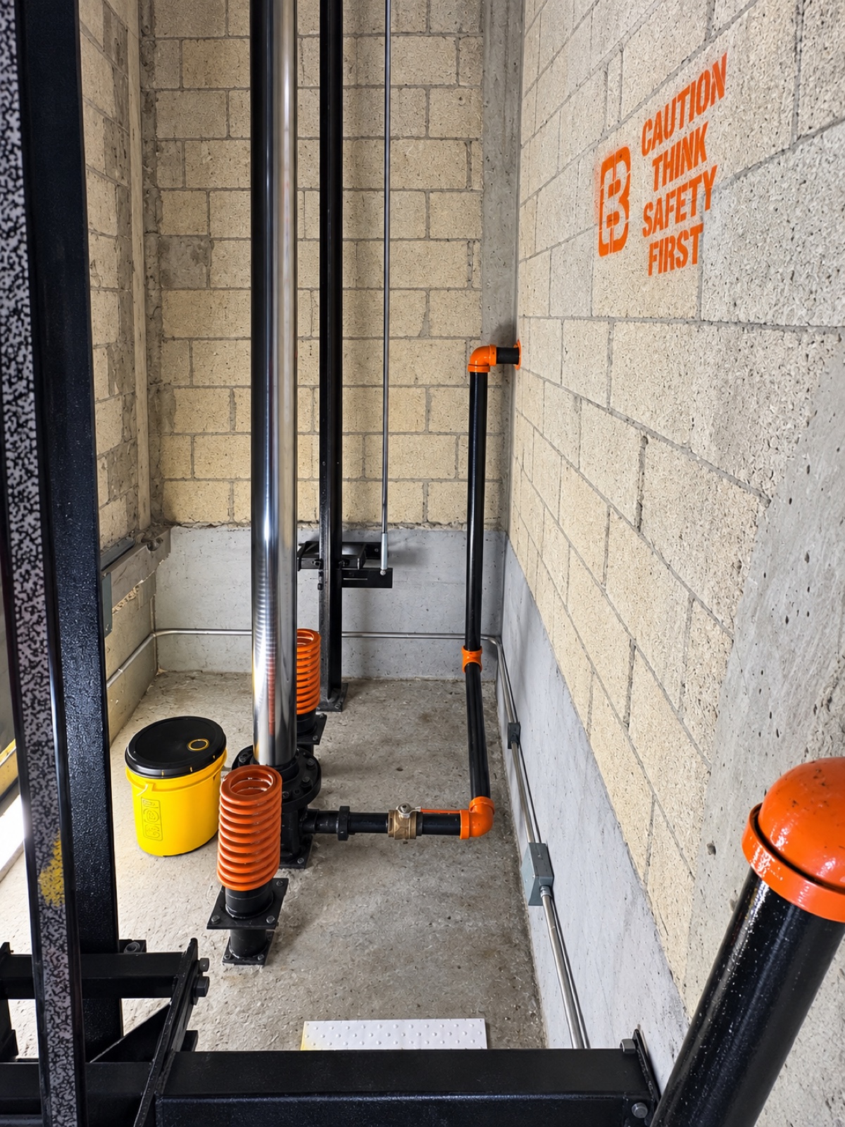 Elevator pit at 1140 Towers in Hialeah after a deep cleaning by Brouss Elevators, with the jack, buffer springs and the Brouss safety stencil on the wall