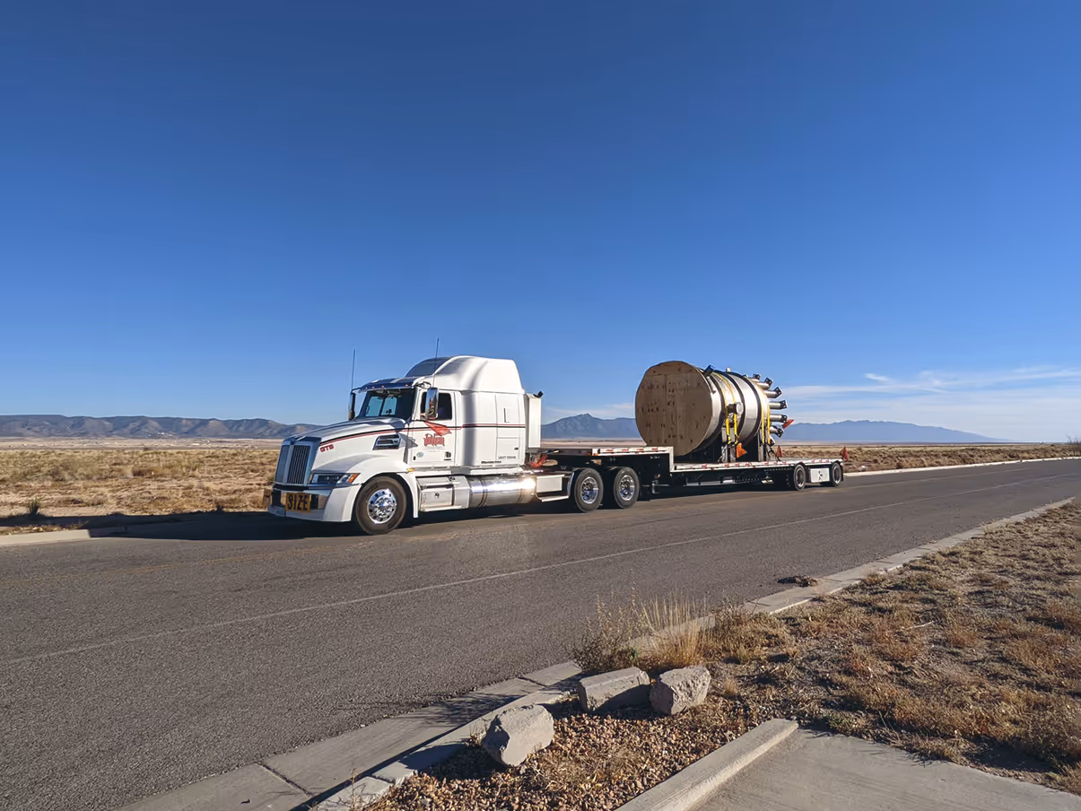 Truck with large vessel on trailer driving down highway