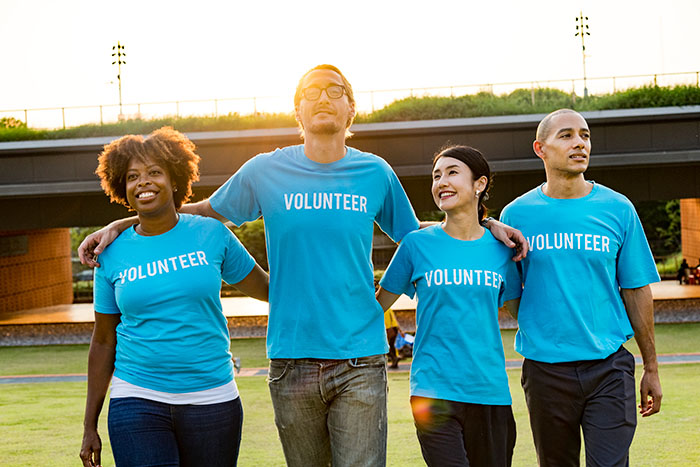 Group of four smiling volunteers wearing matching blue shirts walking together outdoors.