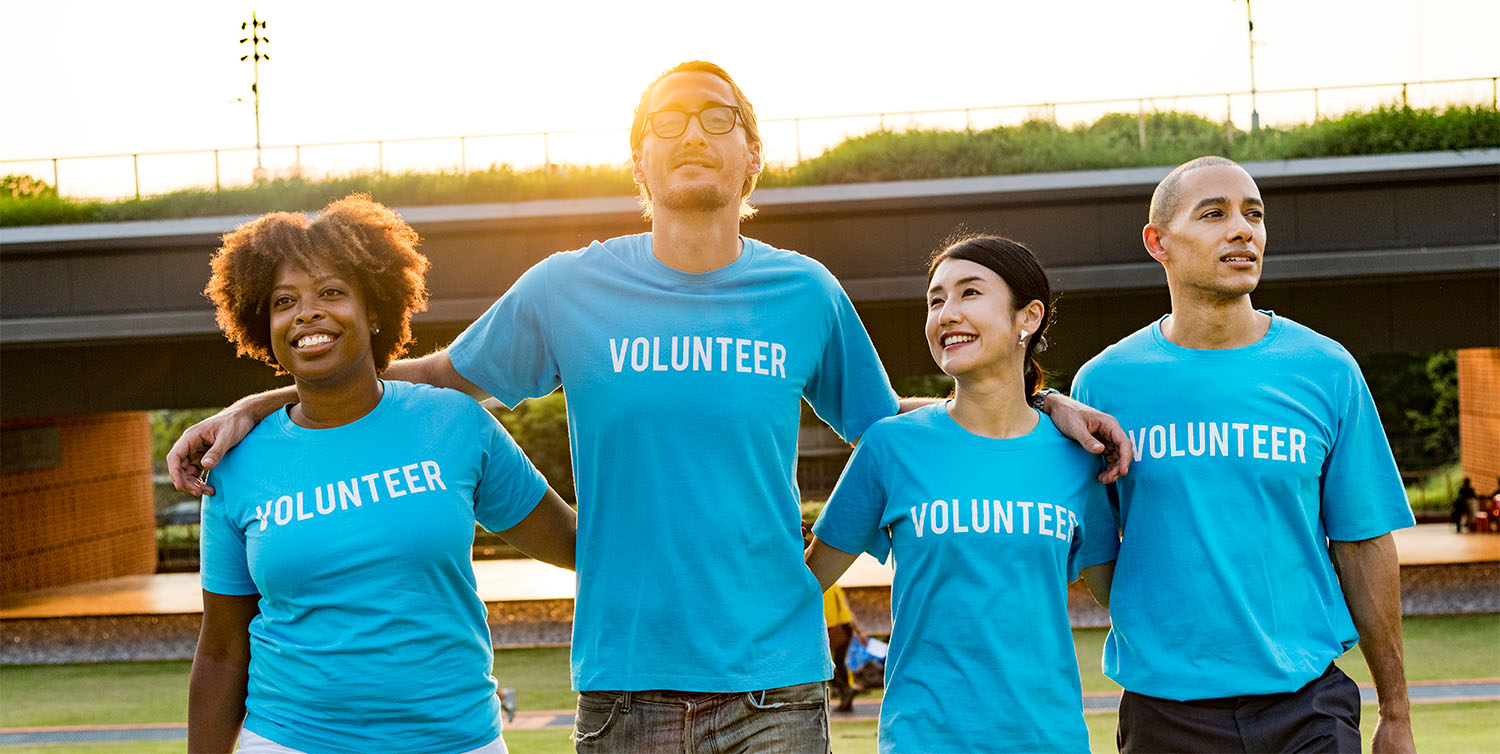 Group of four smiling volunteers wearing matching blue shirts walking together outdoors.