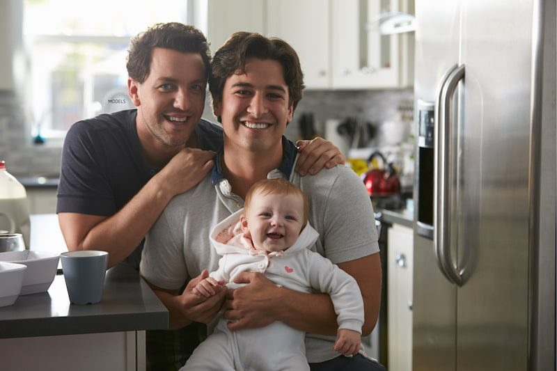 Two men sitting at a kitchen counter with a baby.