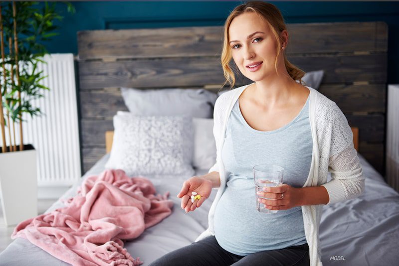 A pregnant woman holding a collection of vitamins and supplements.