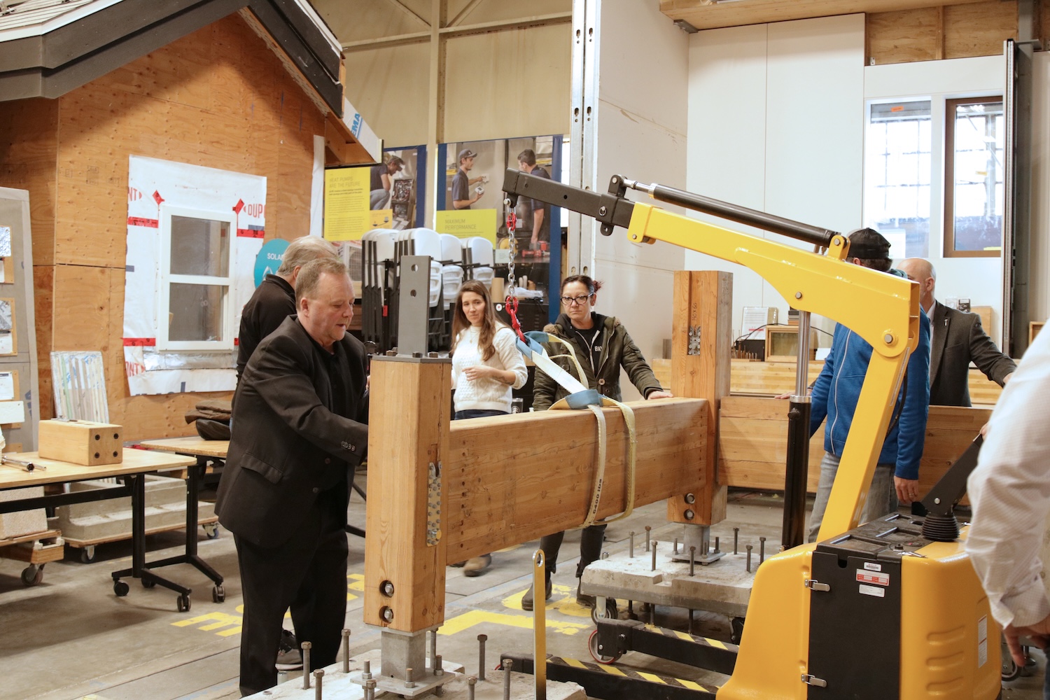 Group of people working with a yellow lifting crane to move a large mass timber beam inside a workshop.