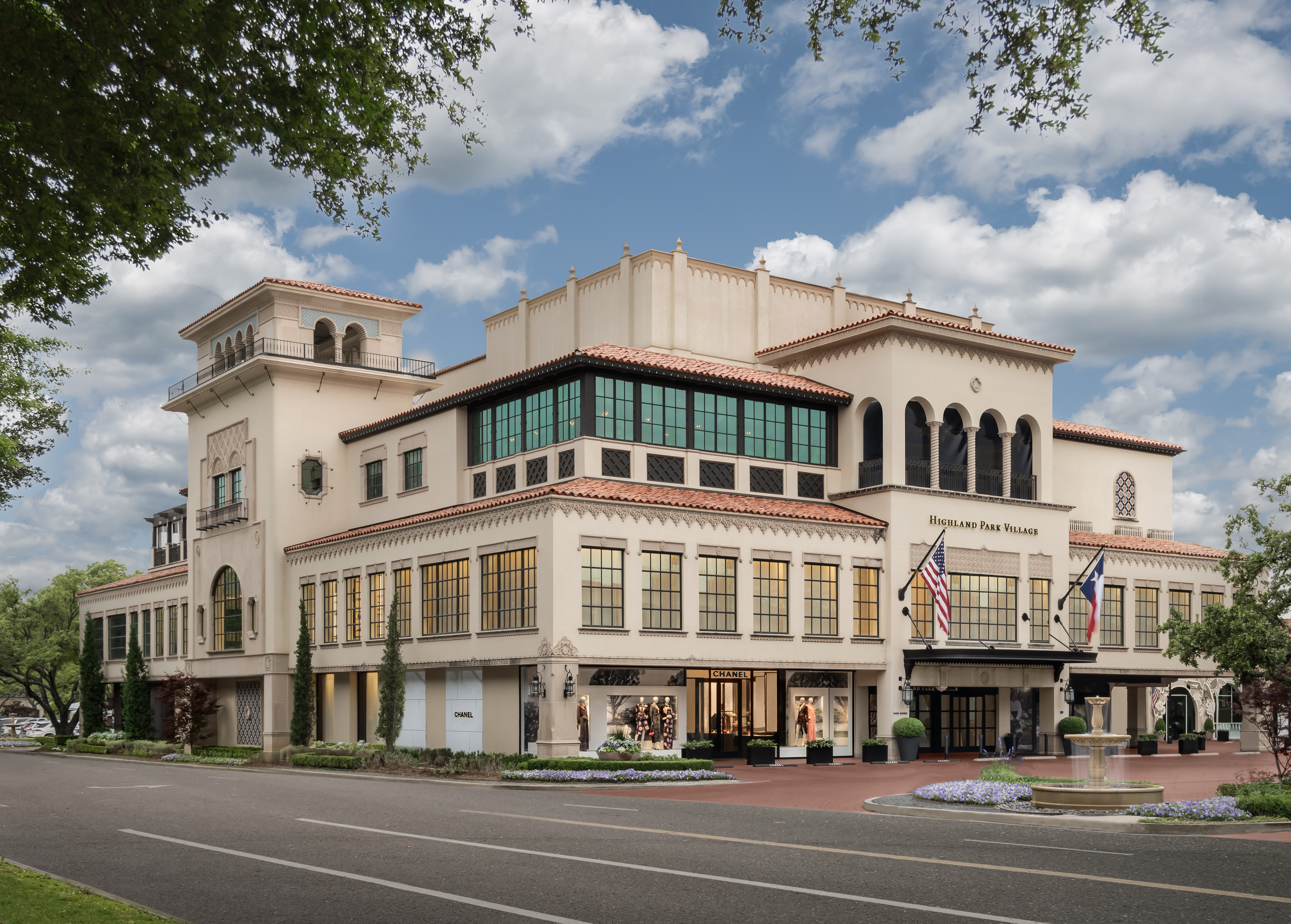 Large Mediterranean-style building housing Highland Park Village with an American and Texas flag at the entrance.