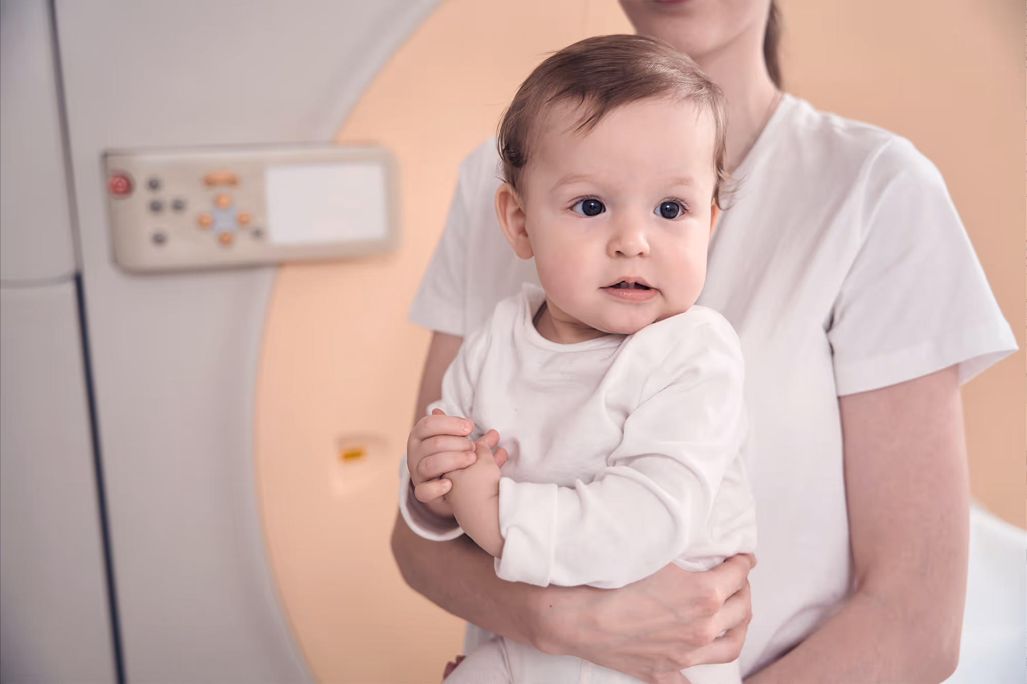 Woman holding baby in front of MRI machine.