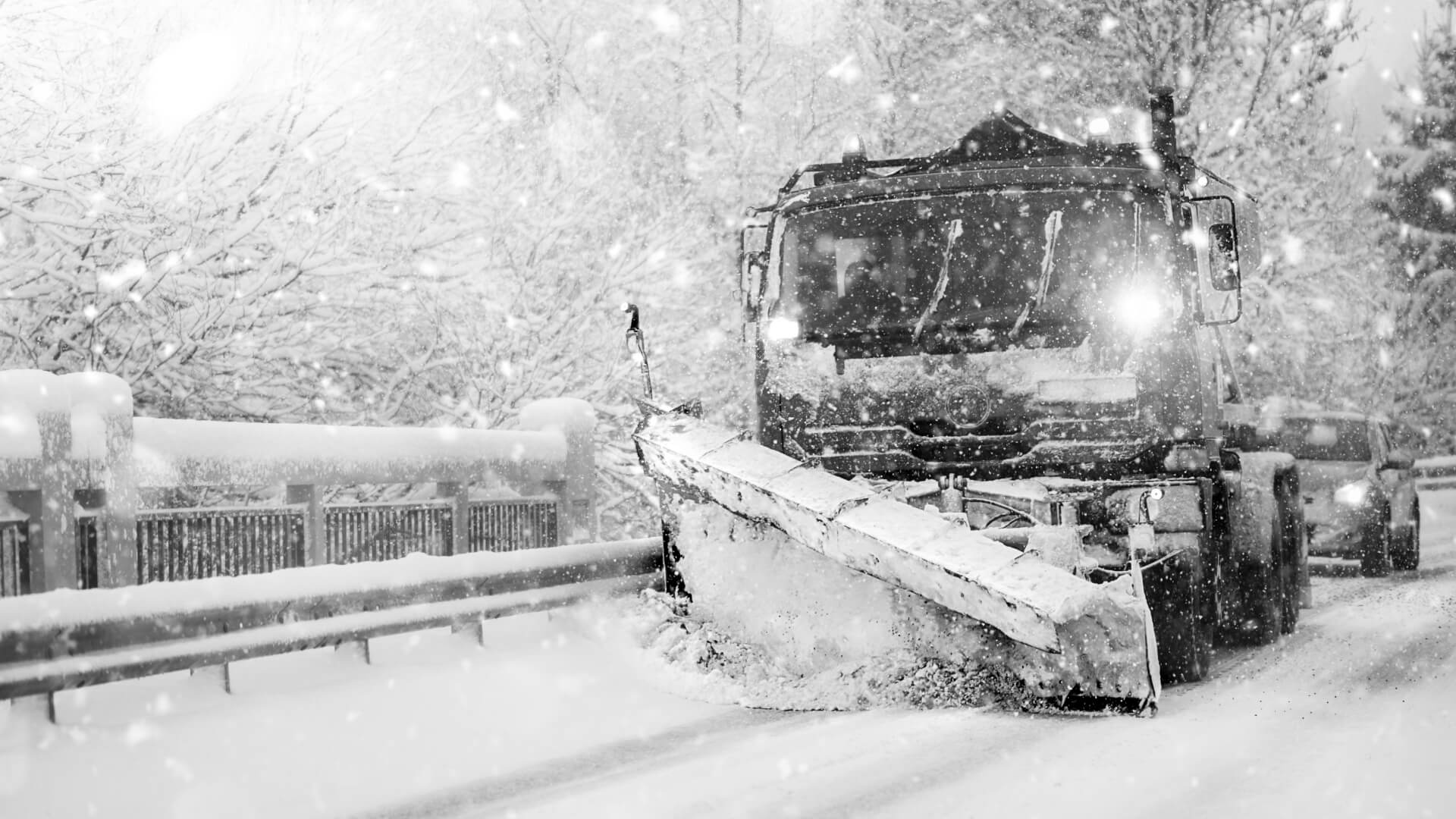 Snow plow clearing road during snowfall.