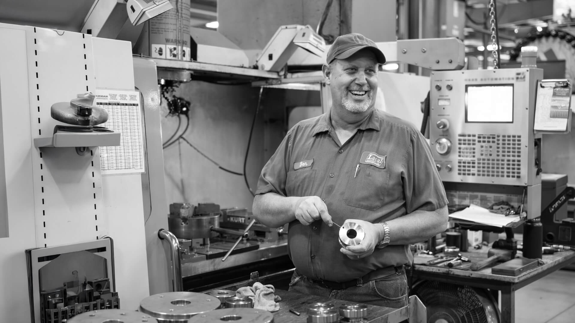 Man working in a machine shop holding a metal part.