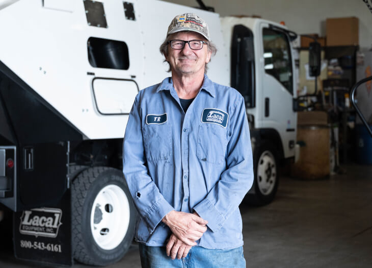 Man standing and smiling in front of street sweeper.