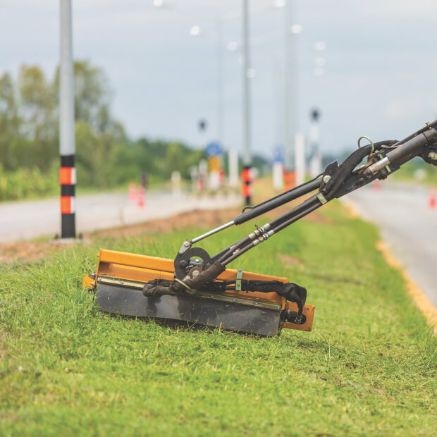 Rotary mower cutting grass along roadside.