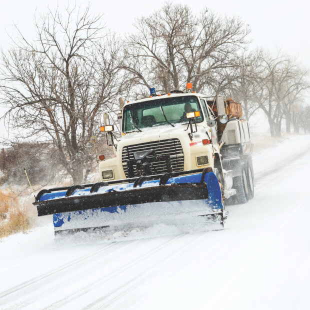 Snow plow clearing road during snowfall.