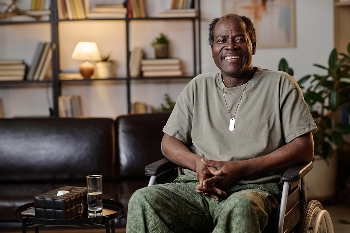 African American senior male sits in a wheelchair dressed in army greens smiling