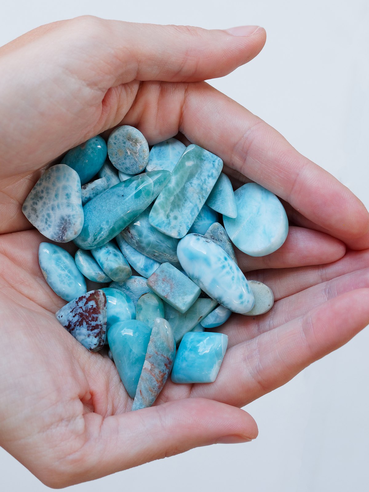 Polished larimar stones held in two hands.