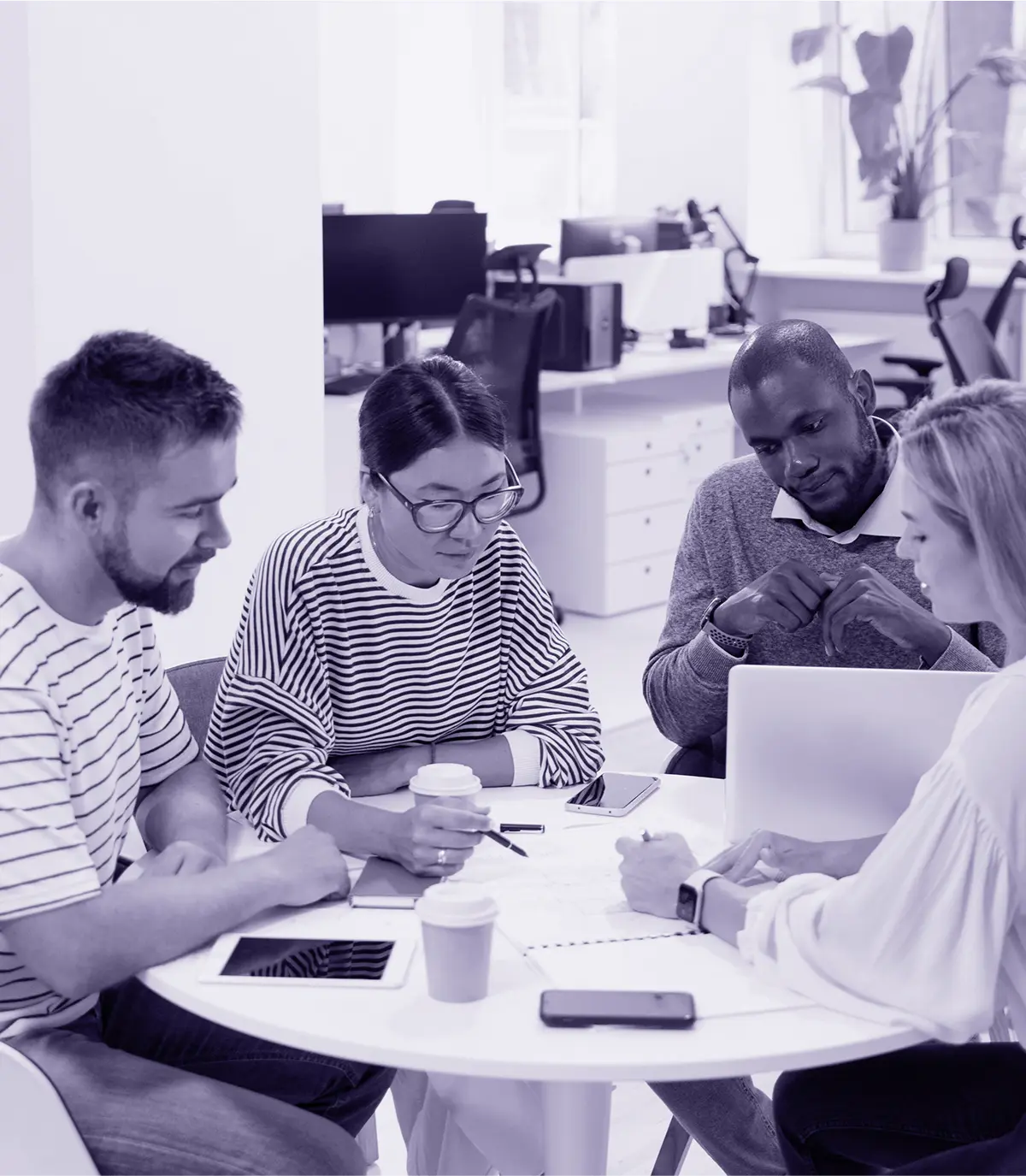Group of four people collaborating at a round table with laptops and coffee cups.