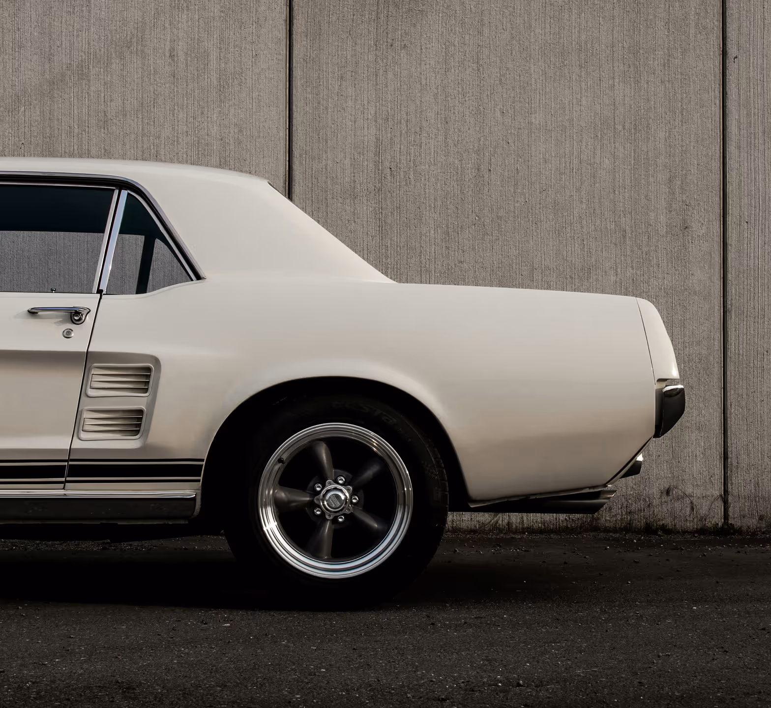 Side view of the rear of a classic white Ford Mustang parked against a concrete wall