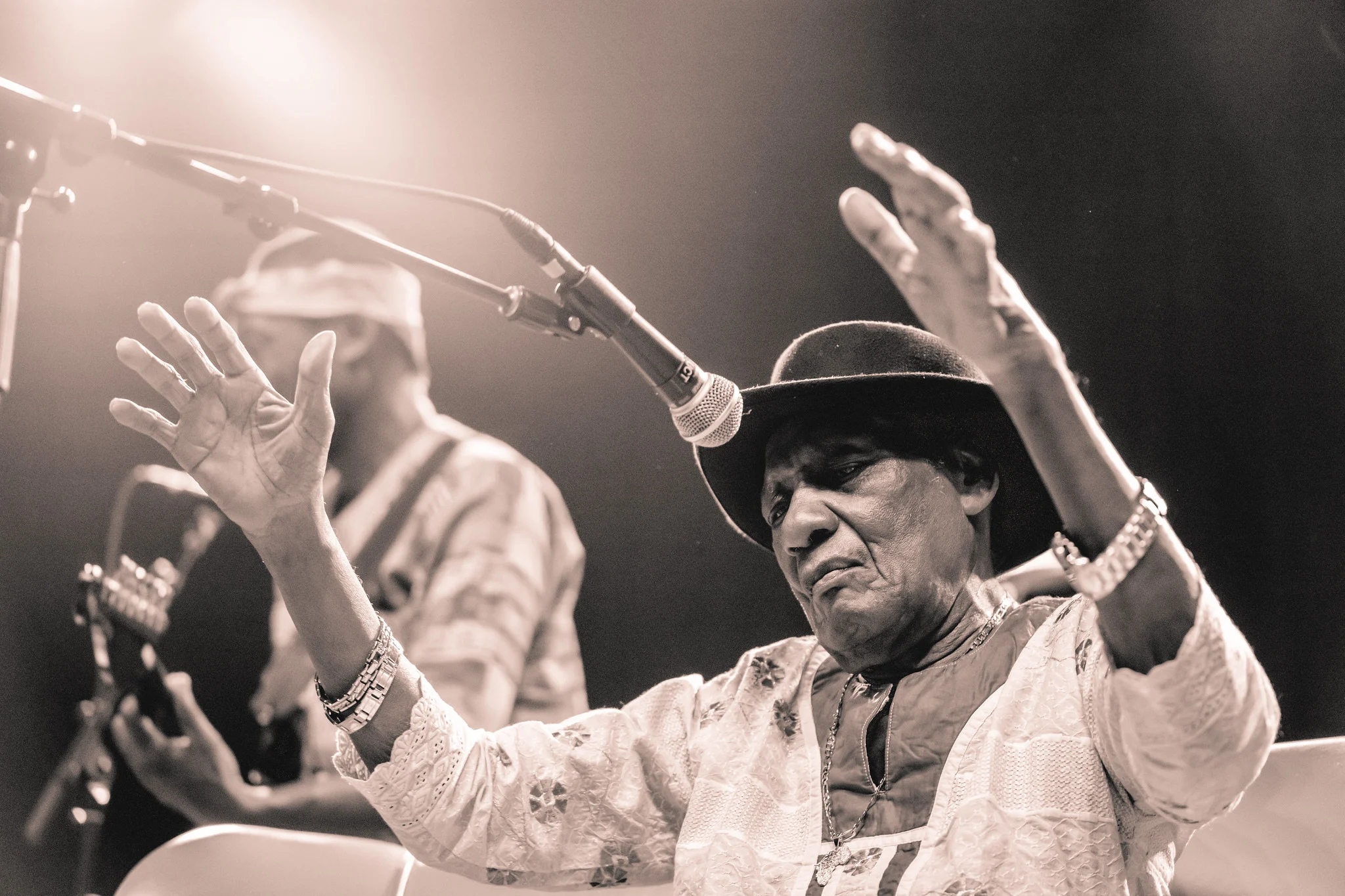 A singer in a black hat raises both hands mid-song