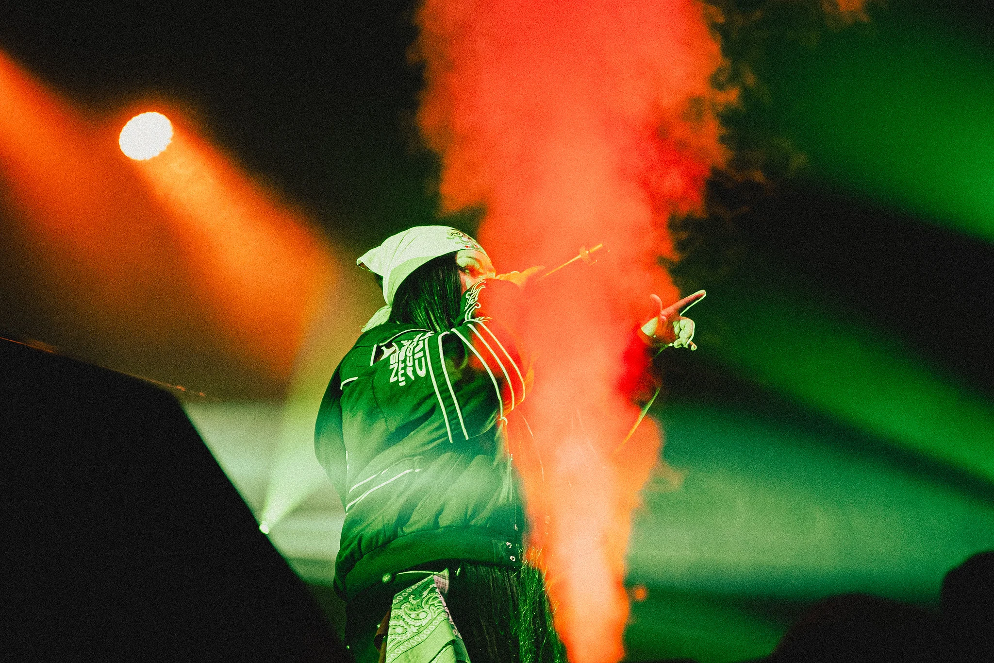 A performer in a white hat sings through a column of red smoke and green stage light