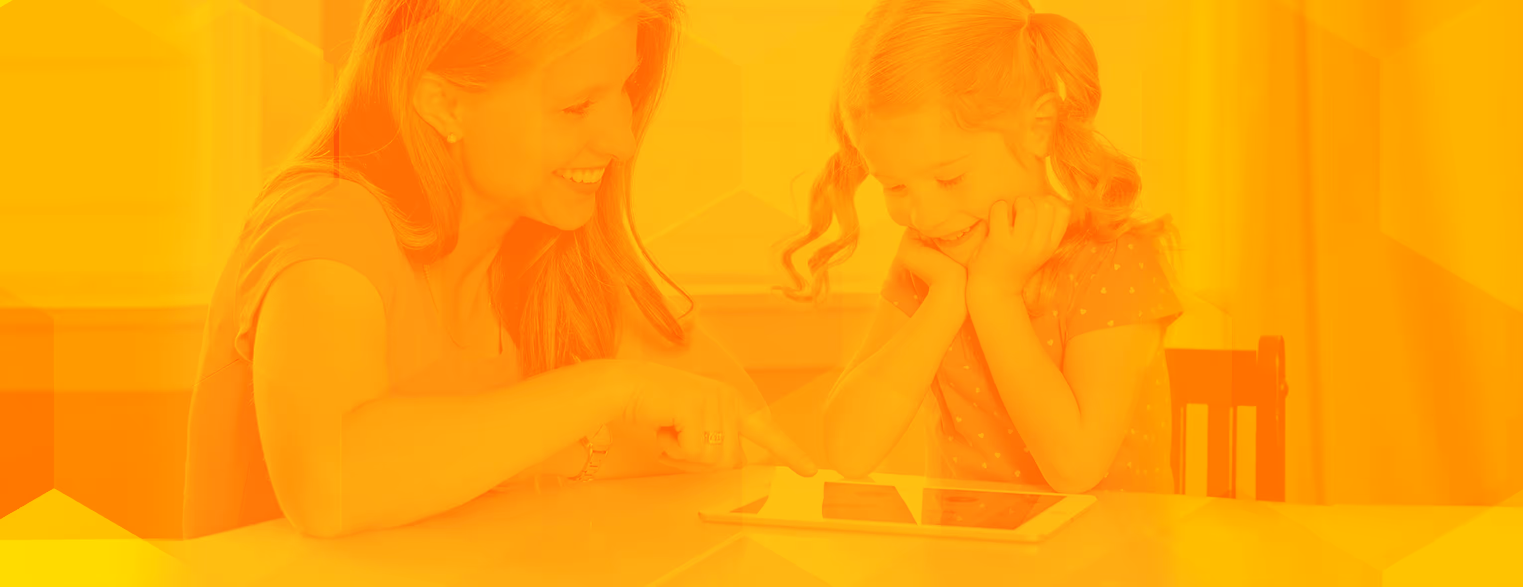 Smiling woman teaching young girl using a tablet at a white table indoors.