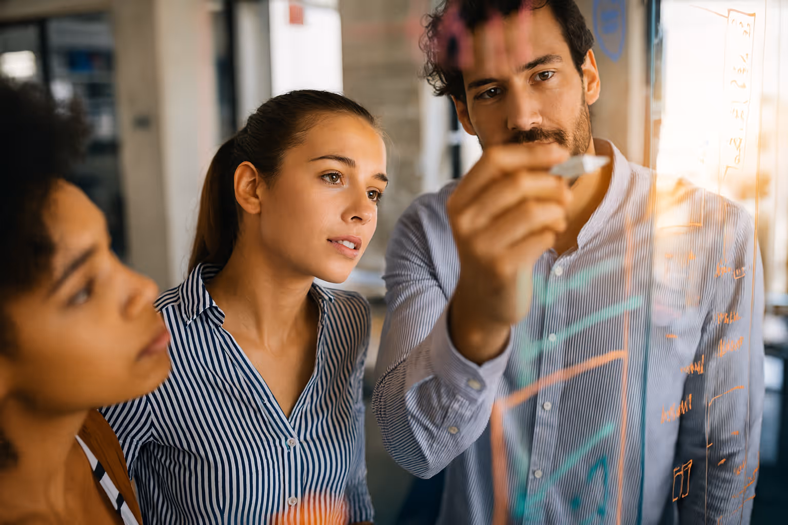 Team of business professionals collaborating on a data strategy, writing on a glass wall to balance AI innovation with privacy compliance.
