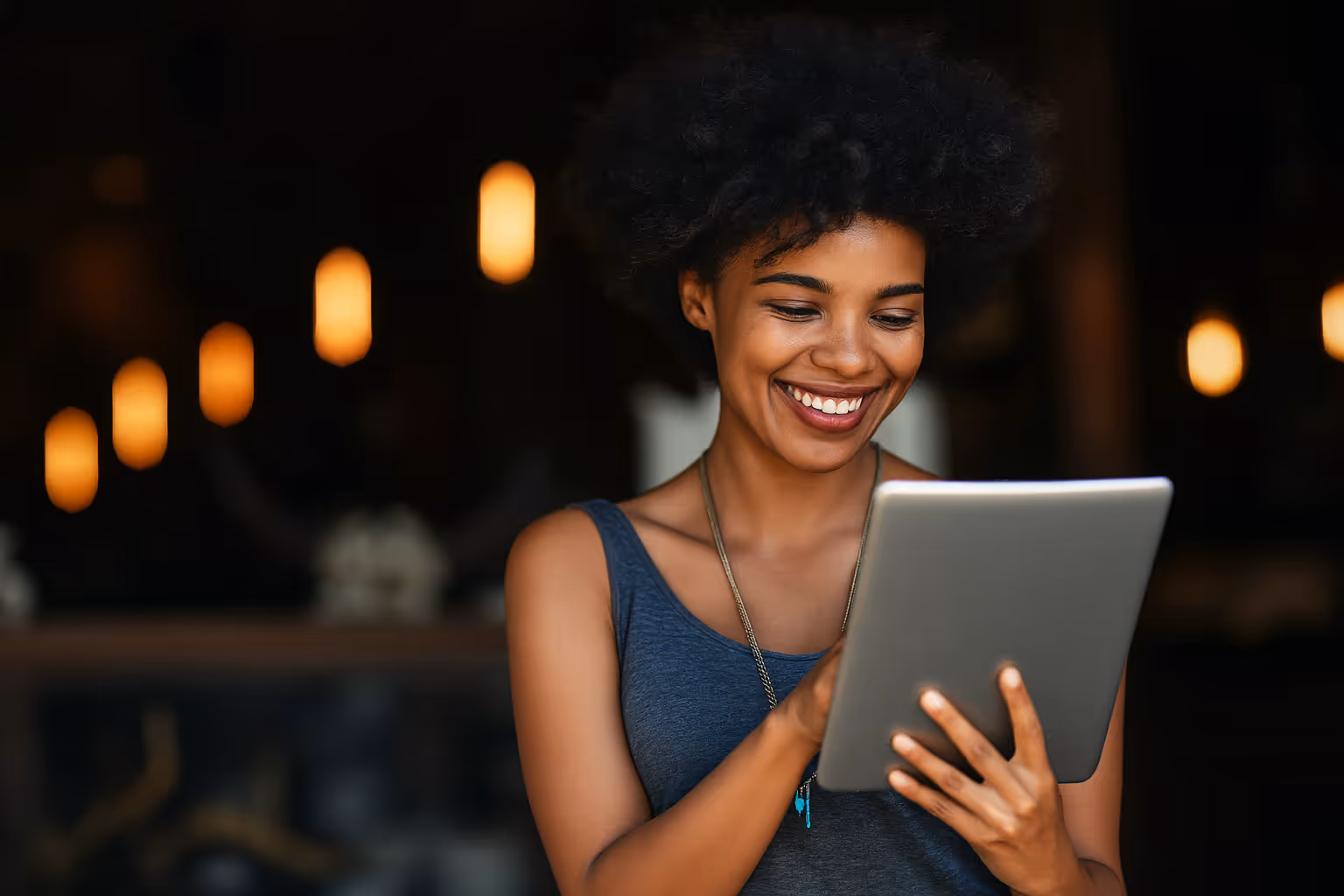 Young woman smiling while using a tablet in a cozy café, symbolizing digital engagement and customer satisfaction.