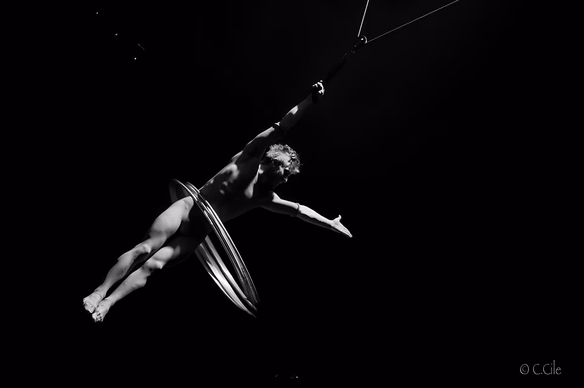 Artiste de cirque suspendu dans les airs, éclairé en clair-obscur, effectuant une figure acrobatique avec des cerceaux.