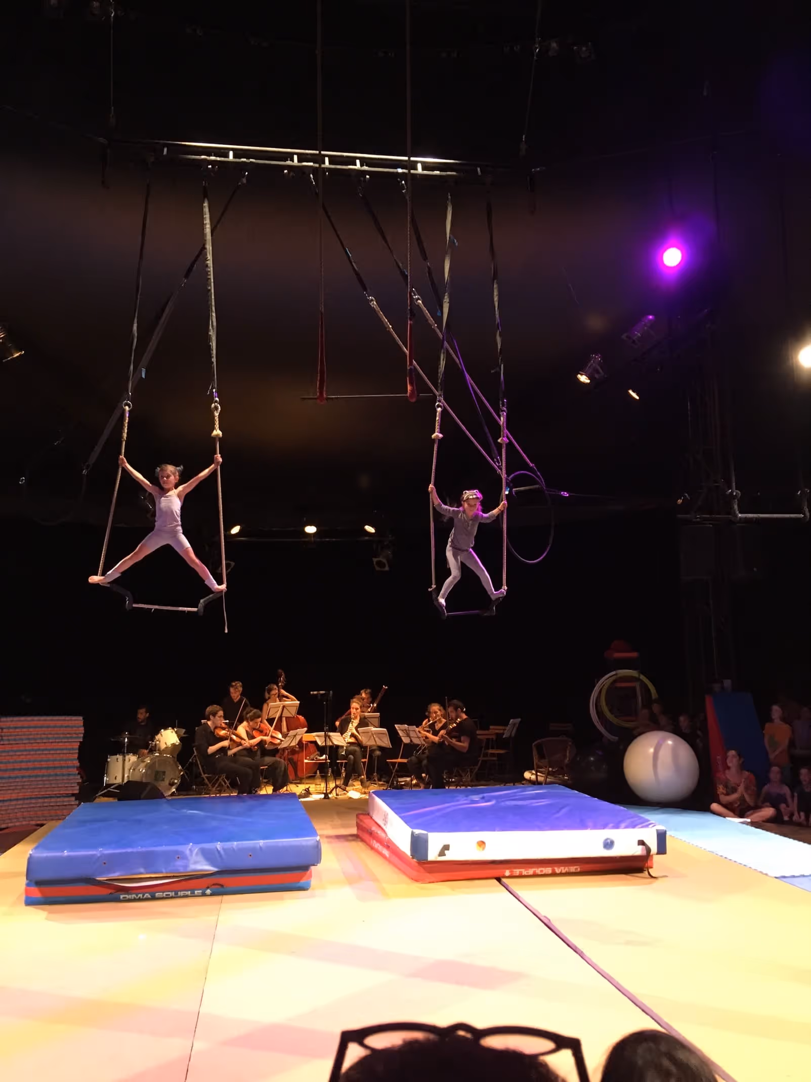 Deux acrobates en herbe en trapèze aérien au-dessus de l'orchestre et du tapis multicolore, spectacle de l'école du Cirque Électrique