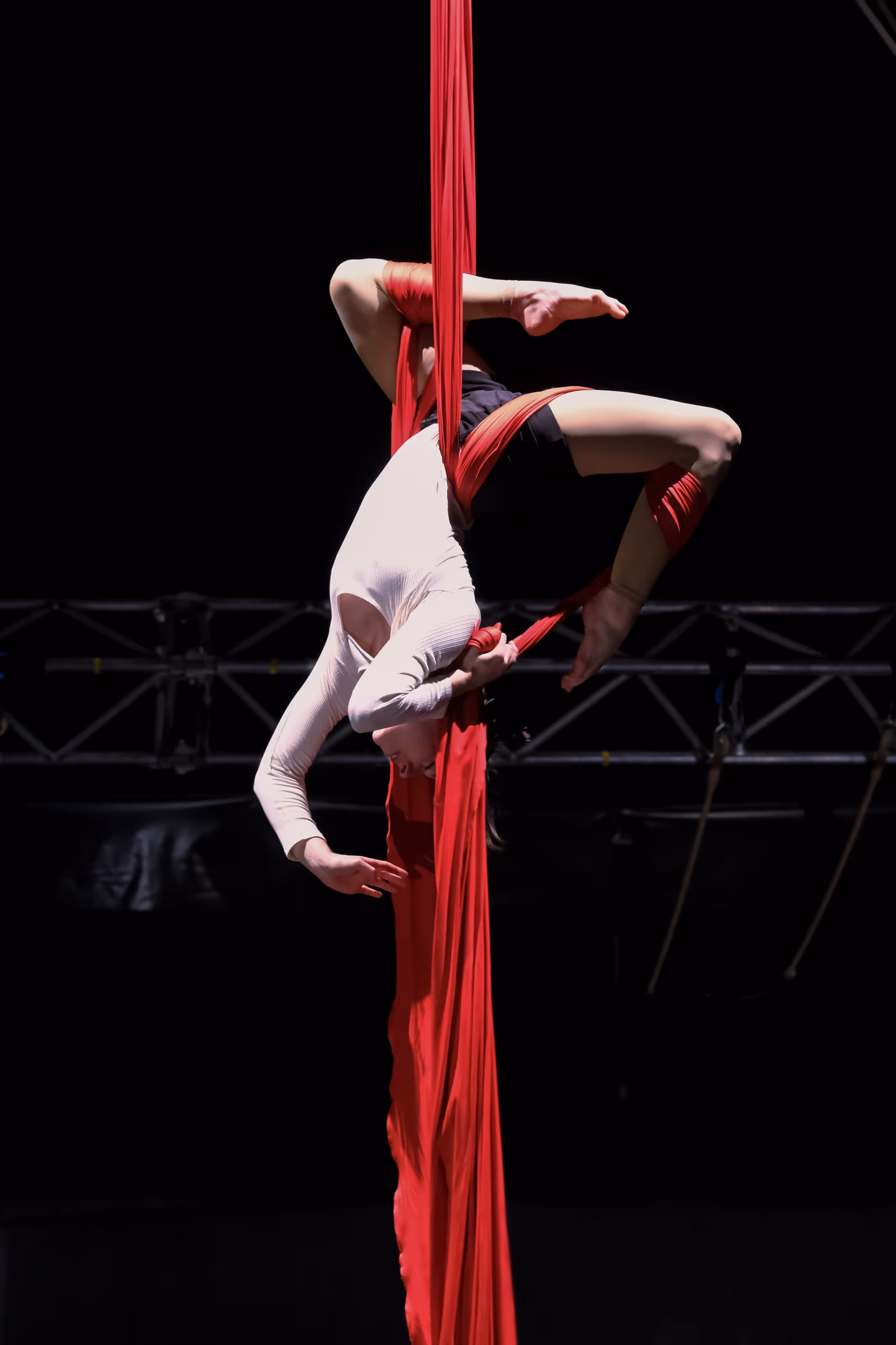 Élève de l'École du Cirque Électrique en suspension sur tissu aérien rouge, corps arqué, performance acrobatique.