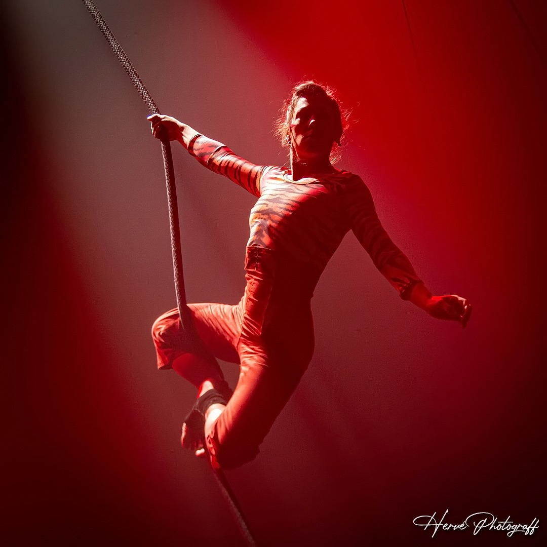Acrobate suspendue à une corde sous éclairage rouge dramatique lors d'un spectacle du Cirque Électrique, photographie de Hervé Photograff