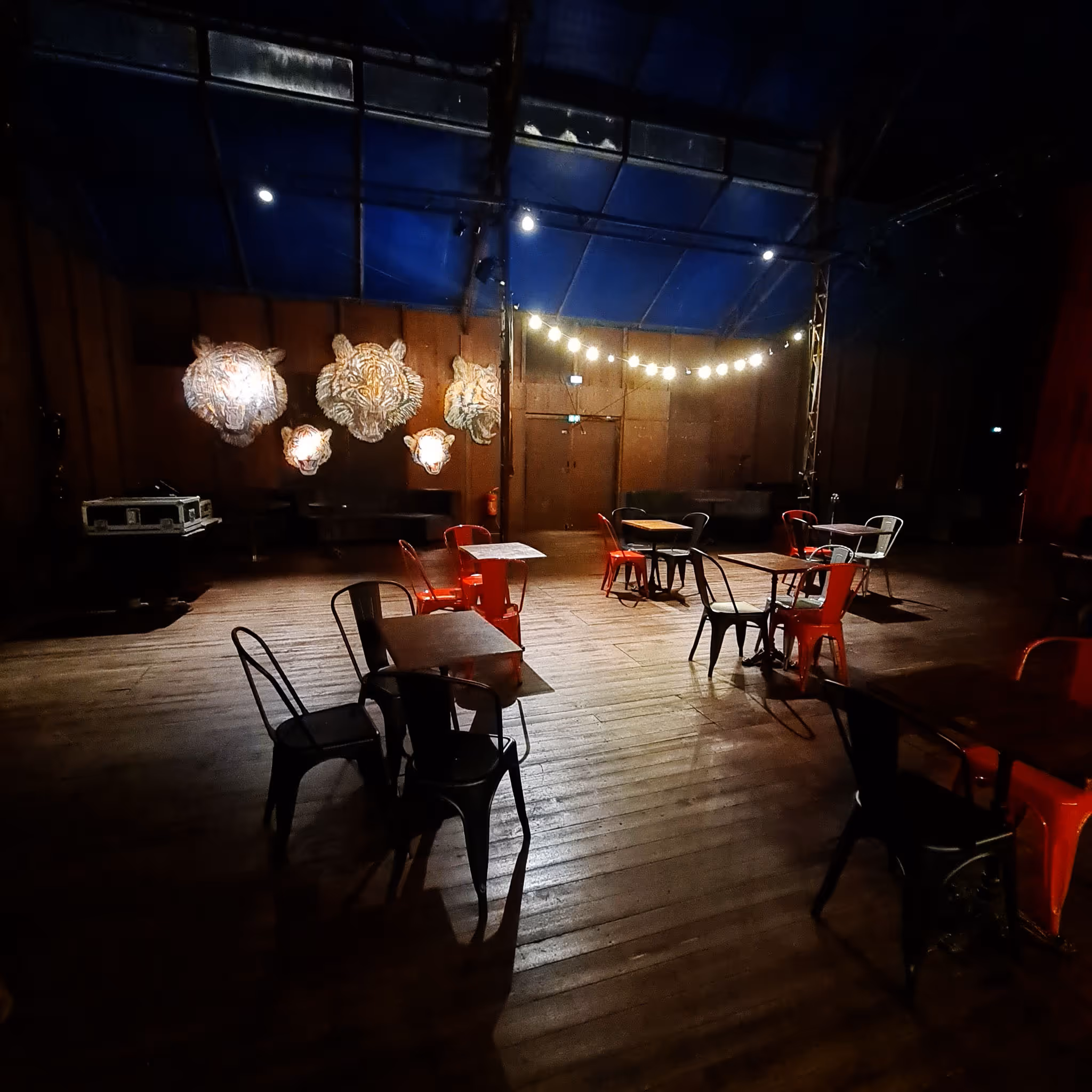 Parquet de bal avec tables et chaises en métal rouges et noires, décor de têtes de tigre lumineuses sur le mur en bois.