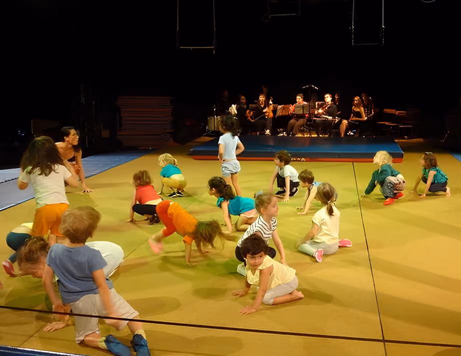 Un groupe d'enfants participe à une activité physique sur un tapis jaune avec un orchestre jouant en arrière-plan.