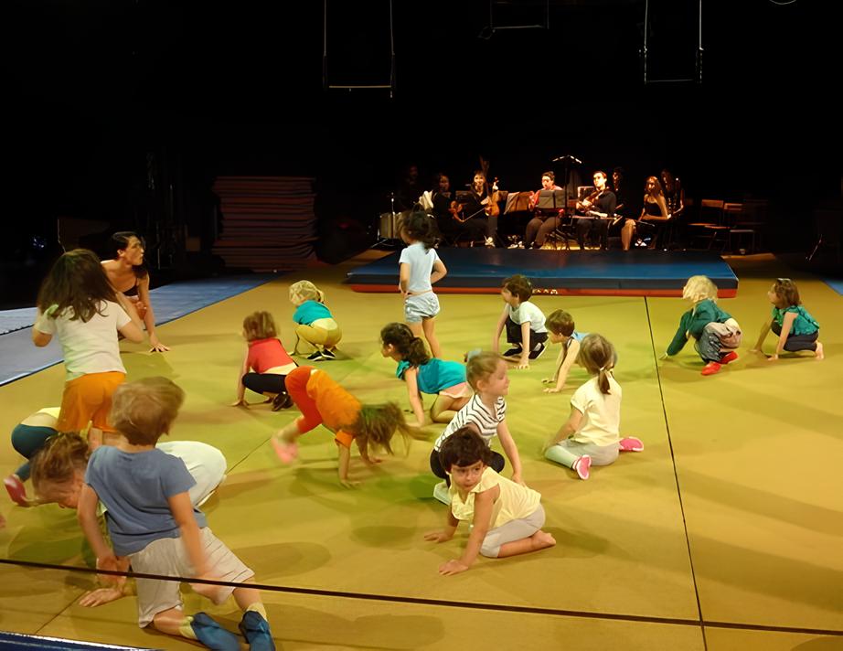 Un groupe d'enfants participe à une activité physique sur un tapis jaune avec un orchestre jouant en arrière-plan.