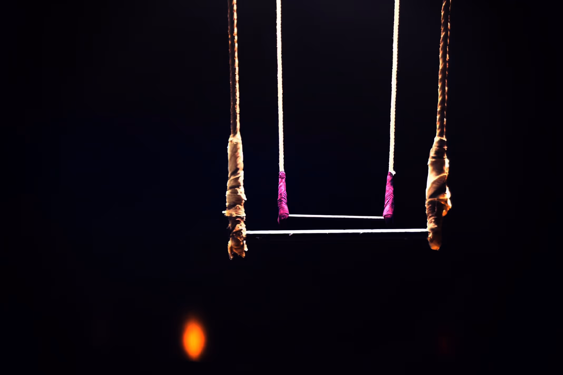 Trapèze de cirque éclairé suspendu dans un environnement sombre.